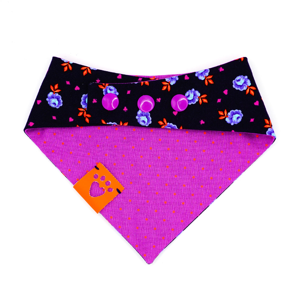 Reversible bandana for dogs. Snaps on back make it adjustable. One side is Navy blue background with purple and light blue rose buds, bright orange leaves and bright purple accent shapes and the other side has Bright purple background with bright orange dots. Orange tag with heart paw cut out on side.