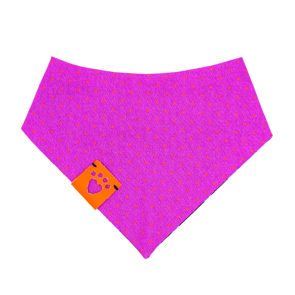 Reversible bandana for dogs. Snaps on back make it adjustable. One side is Navy blue background with purple and light blue rose buds, bright orange leaves and bright purple accent shapes and the other side has Bright purple background with bright orange dots. Orange tag with heart paw cut out on side.