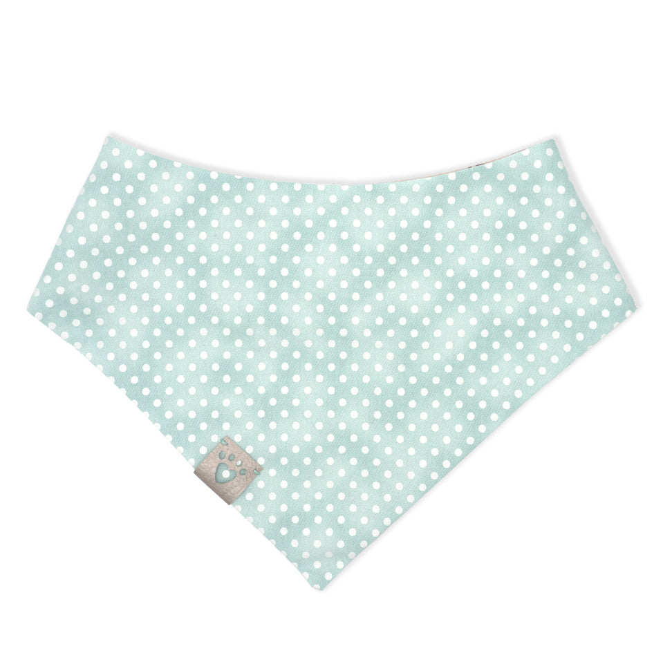 Reversible bandana for dogs. Snaps on back make it adjustable. One side is Distressed minty blue background with white polka dots and the other side has a Very light beige background with brown gingerbread people, some wearing red or black party hats, some with teal pants. Metallic silver tag with heart paw cut out on side.