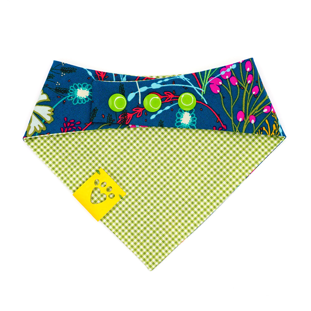 Reversible bandana for dogs. Snaps on back make it adjustable. One side is Dark green/teal background with magenta, dark purple, lime green, white, light blue, goldenrod, and orange flowers and the other side has a Bright lime green and white gingham pattern. Yellow tag with heart paw cut out on side.