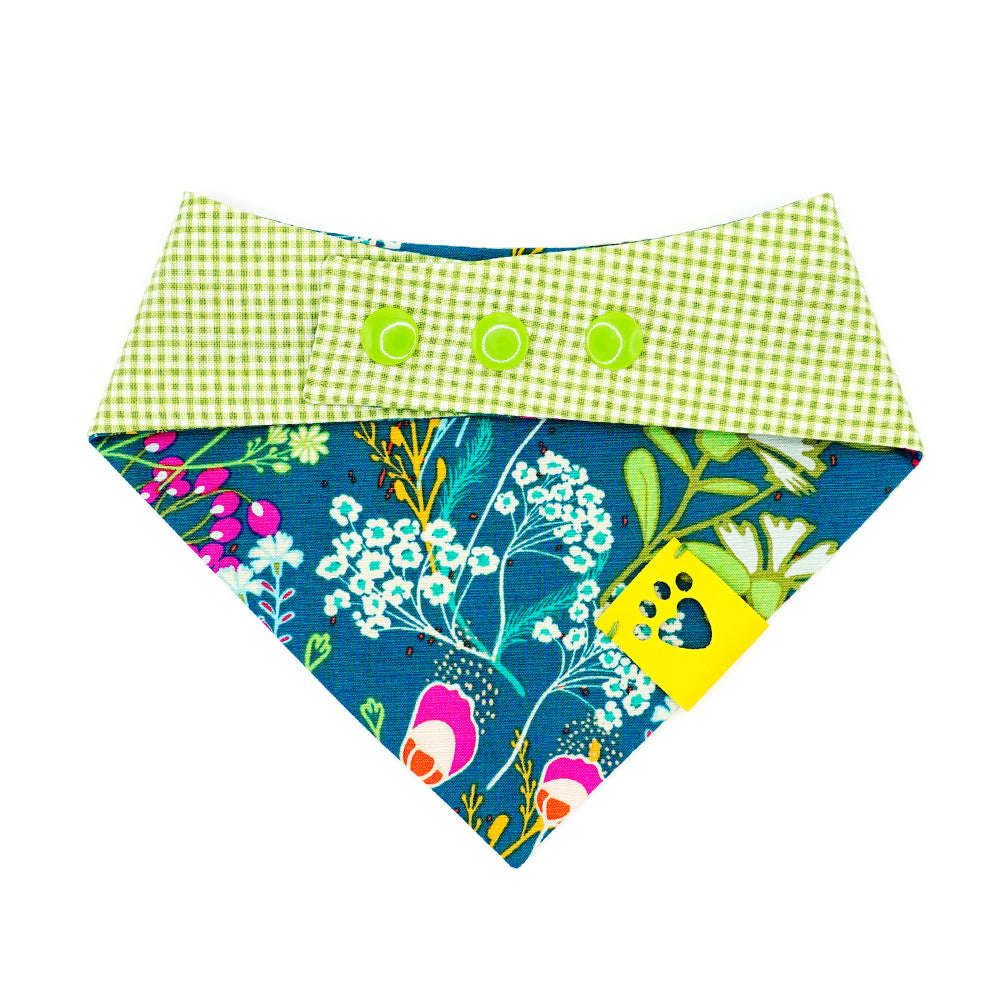 Reversible bandana for dogs. Snaps on back make it adjustable. One side is Dark green/teal background with magenta, dark purple, lime green, white, light blue, goldenrod, and orange flowers and the other side has a Bright lime green and white gingham pattern. Yellow tag with heart paw cut out on side.