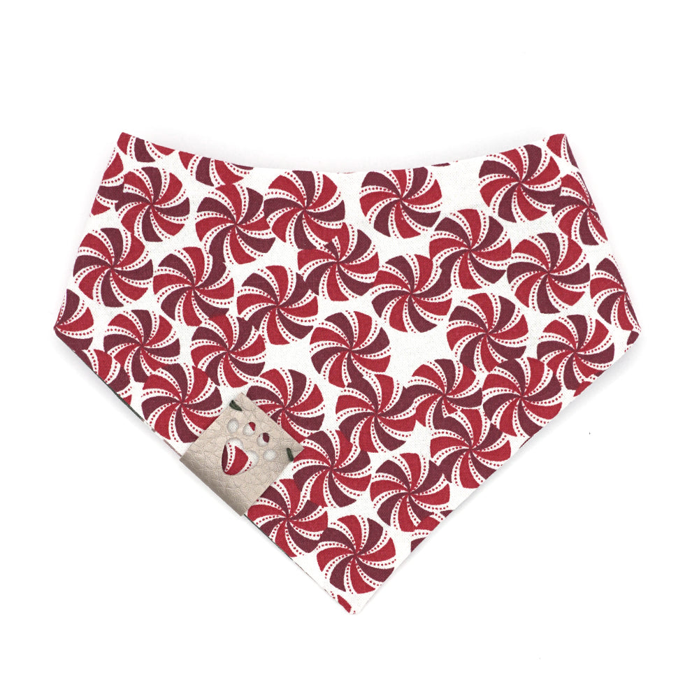Reversible bandana for dogs. Snaps on back make it adjustable. One side is Dark green background with brown gingerbread houses/people, white icing, snowflakes, and multi-colored candies and decorations and the other side has a White background with dark red, red and white peppermint swirl candies. Metallic Silver tag with heart paw cut out on side.