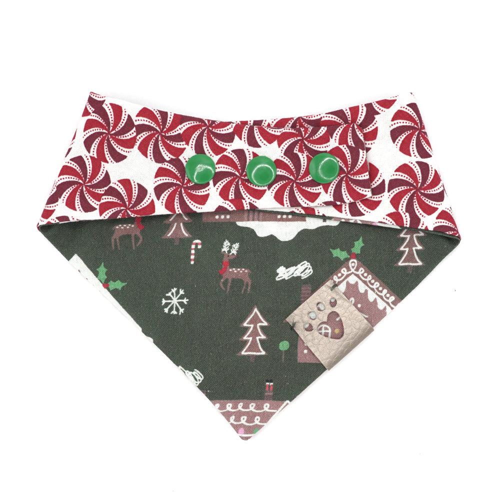 Reversible bandana for dogs. Snaps on back make it adjustable. One side is Dark green background with brown gingerbread houses/people, white icing, snowflakes, and multi-colored candies and decorations and the other side has a White background with dark red, red and white peppermint swirl candies. Metallic Silver tag with heart paw cut out on side.