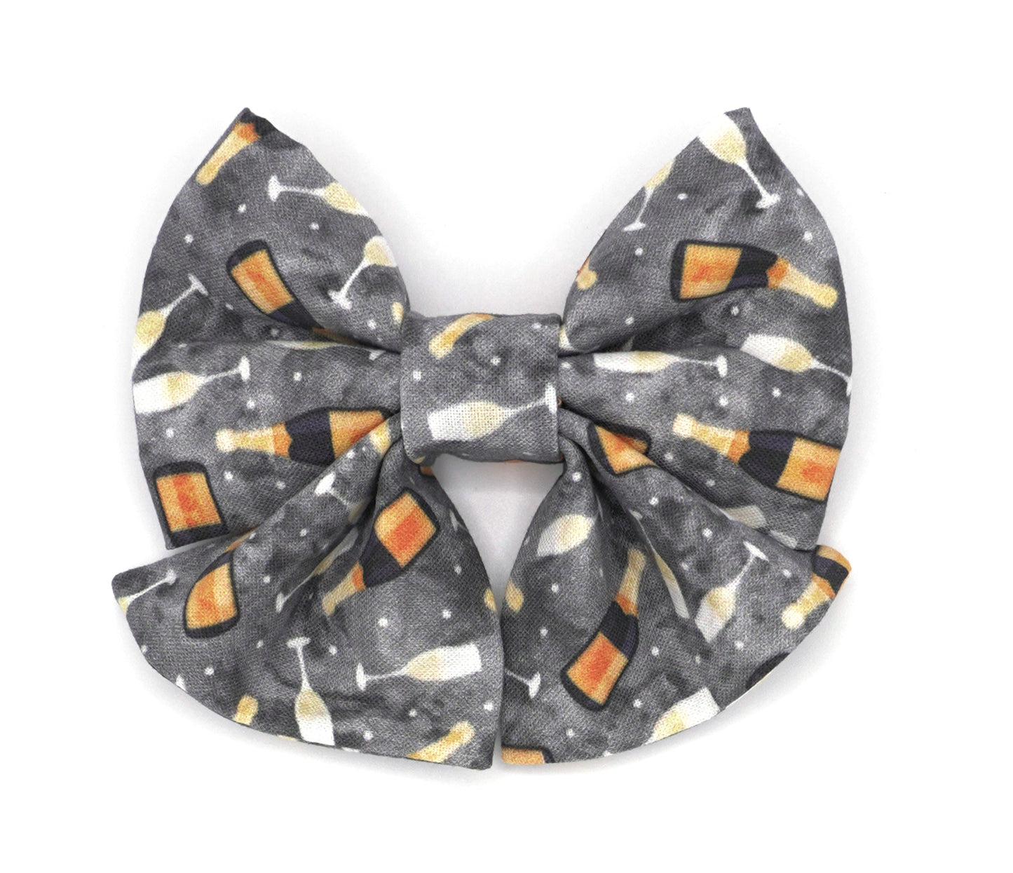 Handmade cotton bow tie with tails for dogs (or other pets). Elastic straps on back with snaps make it easy to add to collar, harness, or leash. Grey background with sparkling wine bottles and glasses.