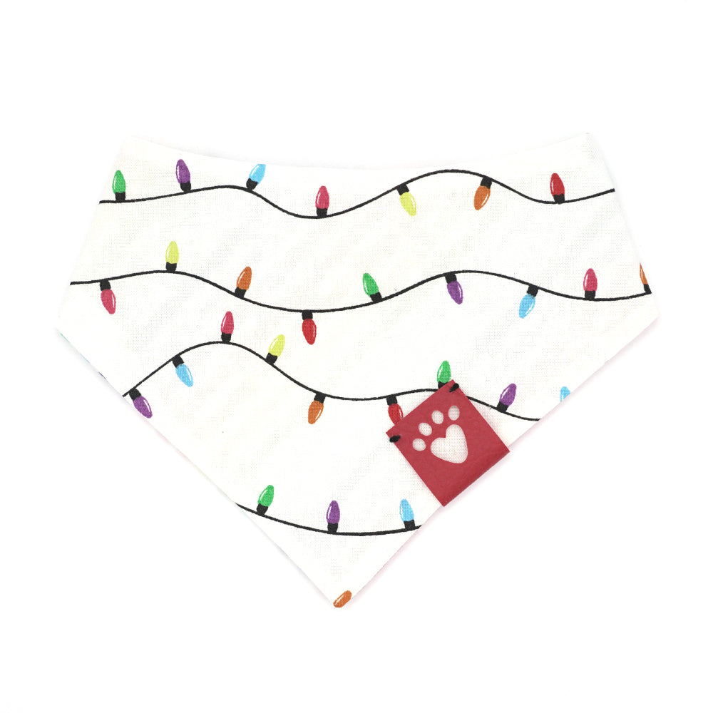 Reversible bandana for dogs. Snaps on back make it adjustable. One side is White background with rainbow-colored lights on a black cord and the other side has a White background with rainbow stripes. Dark Pink tag with heart paw cut out on side.