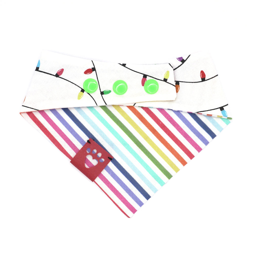 Reversible bandana for dogs. Snaps on back make it adjustable. One side is White background with rainbow-colored lights on a black cord and the other side has a White background with rainbow stripes. Dark Pink tag with heart paw cut out on side.