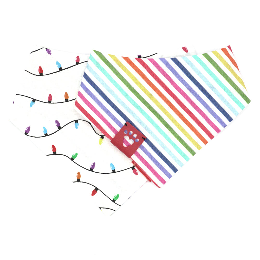Reversible bandana for dogs. Snaps on back make it adjustable. One side is White background with rainbow-colored lights on a black cord and the other side has a White background with rainbow stripes. Dark Pink tag with heart paw cut out on side.