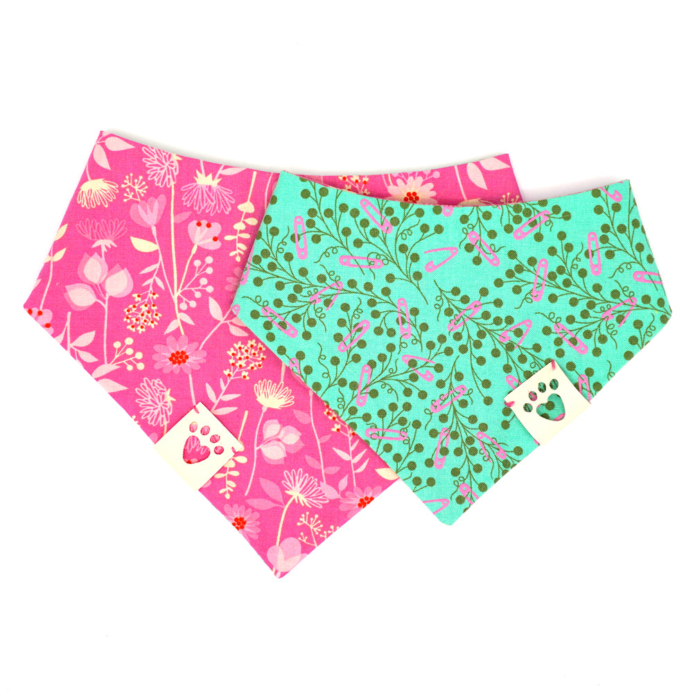 Reversible bandana for dogs. Snaps on back make it adjustable. One side is Teal green background with pink safety pins and dark green flowers and the other side has a Bright pink background with pink, cream and red flowers. Cream tag with heart paw cut out on side.