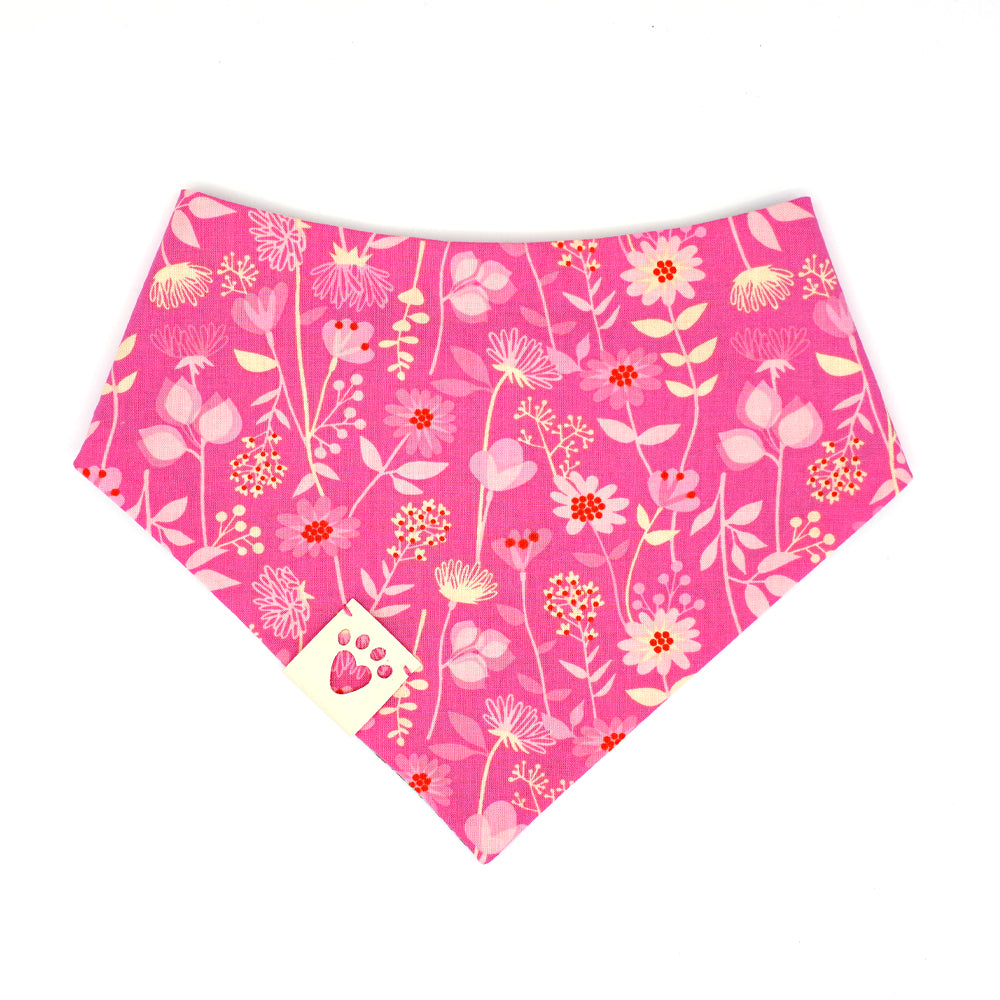 Reversible bandana for dogs. Snaps on back make it adjustable. One side is Teal green background with pink safety pins and dark green flowers and the other side has a Bright pink background with pink, cream and red flowers. Cream tag with heart paw cut out on side.