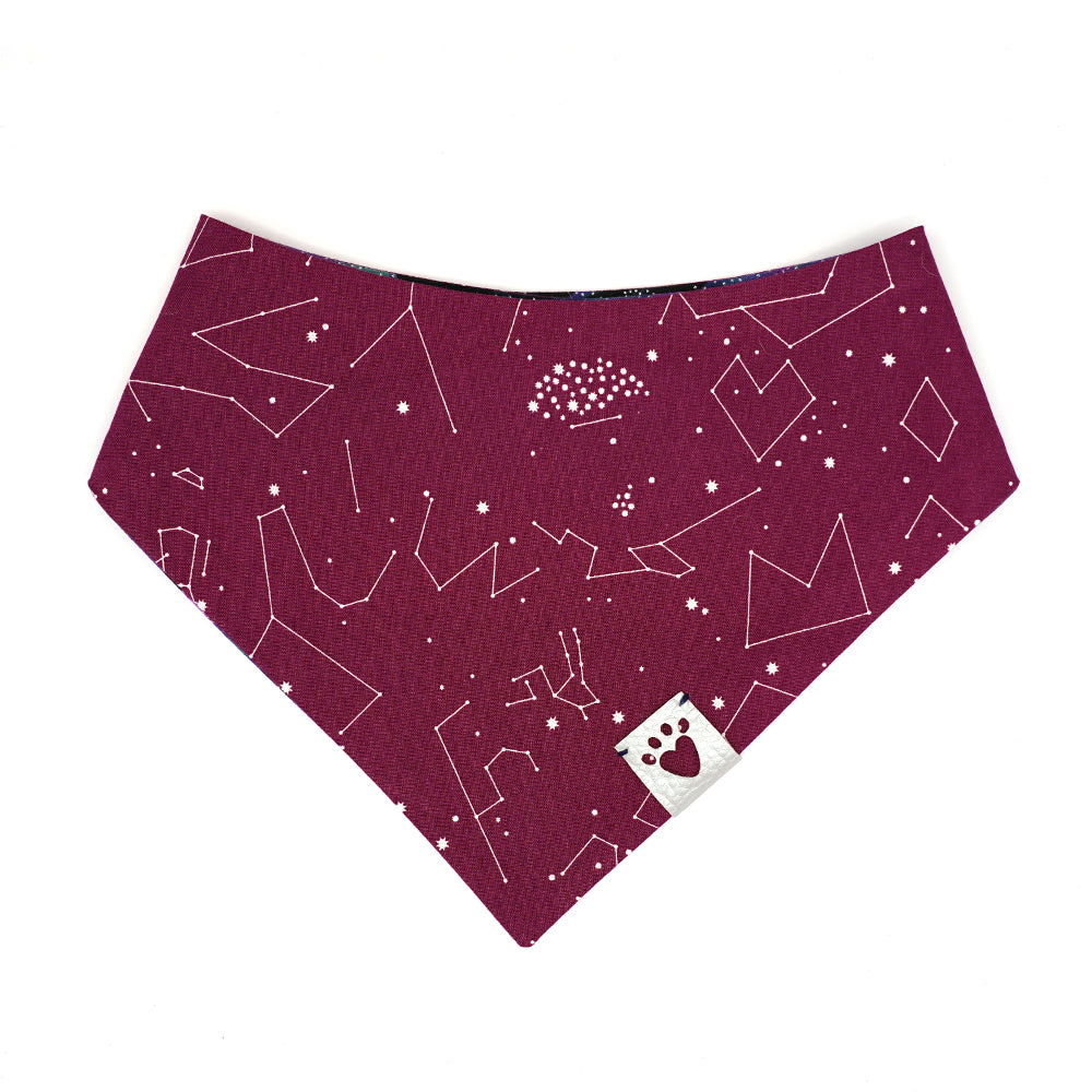 Reversible bandana for dogs. Snaps on back make it adjustable. One side is Black, purple, blue, teal galaxy wave background with silver metallic star dots and the other side has a Purple/wine color background with white constellations and starbursts. Metallic Silver tag with heart paw cut out on side.