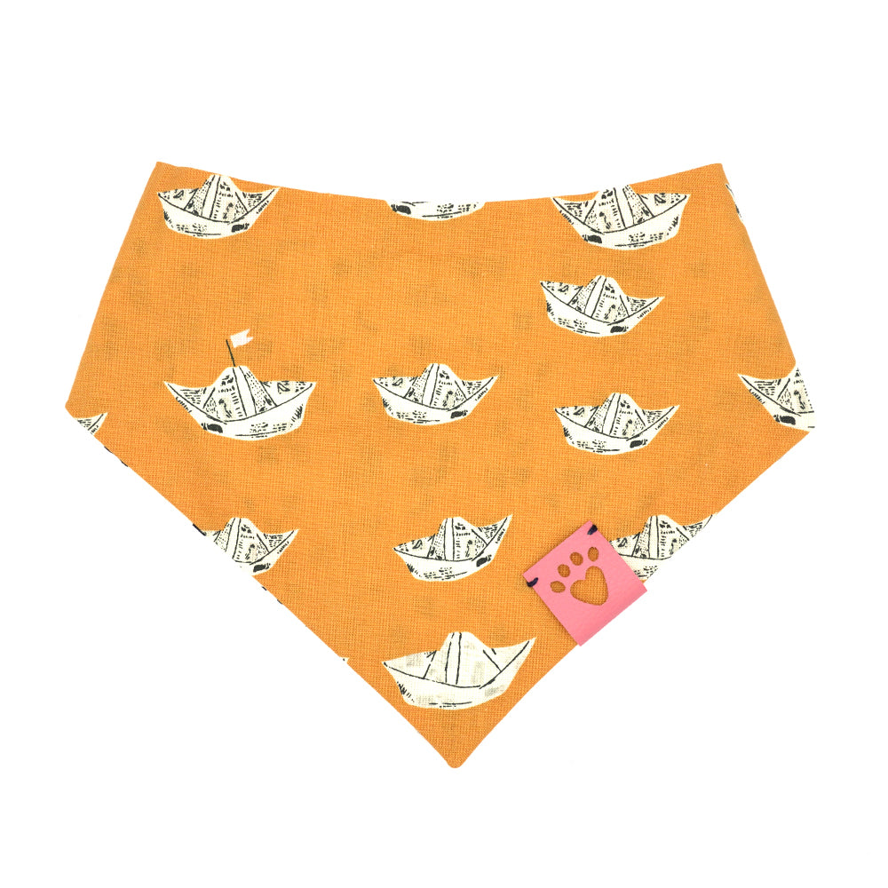 Reversible bandana for dogs. Snaps on back make it adjustable. One side is Bright orange background with newsprint boats and the other side has a White background with black geometric pattern. Light Pink tag with heart paw cut out on side.