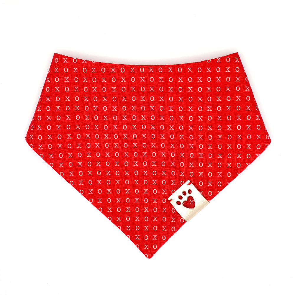 Reversible bandana for dogs. Snaps on back make it adjustable. One side is right red background with white Xs and Os and the other side has a White background with large and small red dots. Metallic Silver tag with heart paw cut out on side.