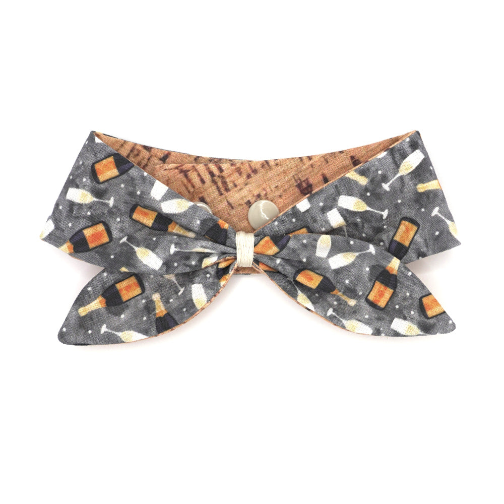 Reversible neckerchief for dogs. Snaps on back make it adjustable. One side is Grey background with sparkling wine bottles and glasses and the other side has a Tan/brown cork pattern. Embroidery thread wrapped center in cream.