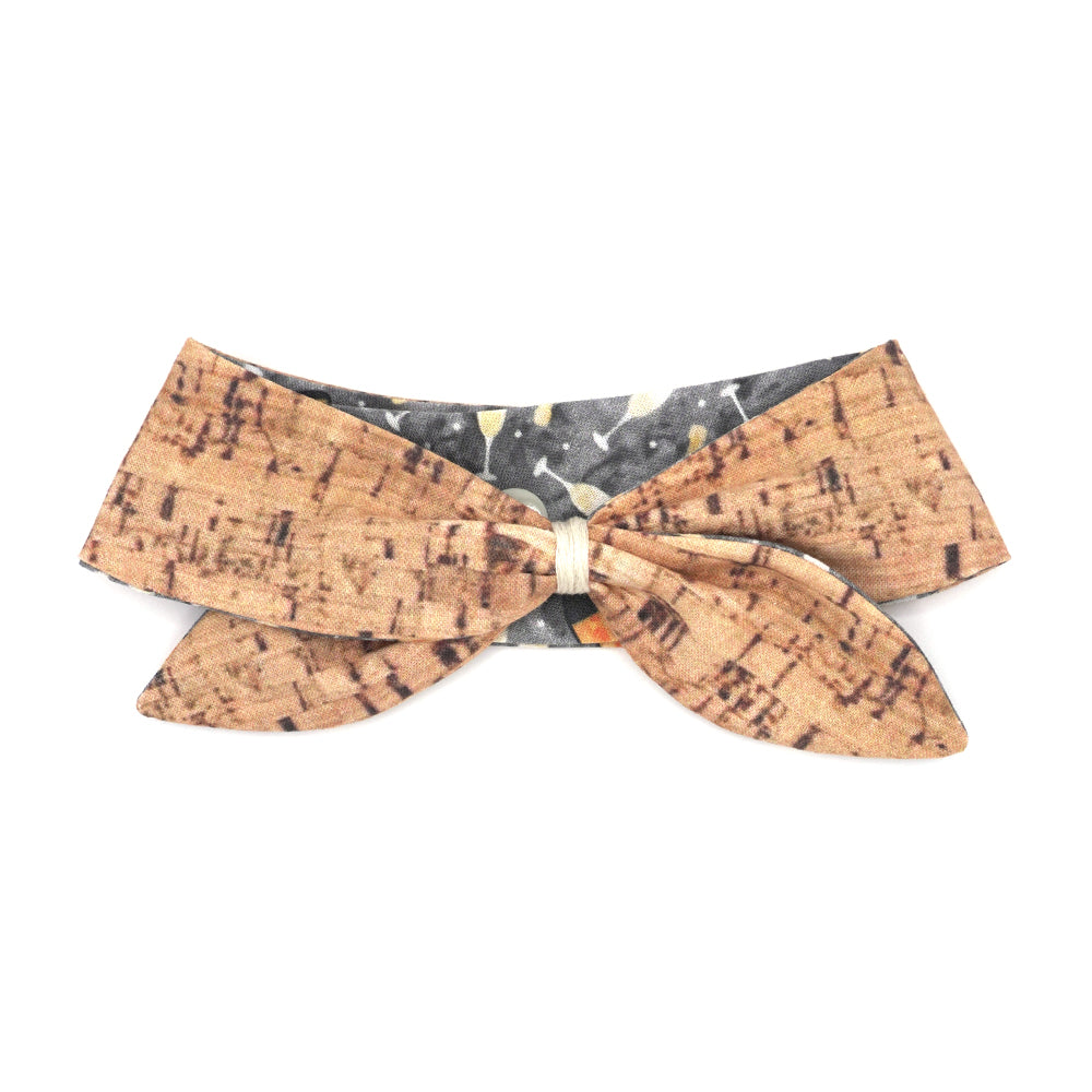Reversible neckerchief for dogs. Snaps on back make it adjustable. One side is Grey background with sparkling wine bottles and glasses and the other side has a Tan/brown cork pattern. Embroidery thread wrapped center in cream.