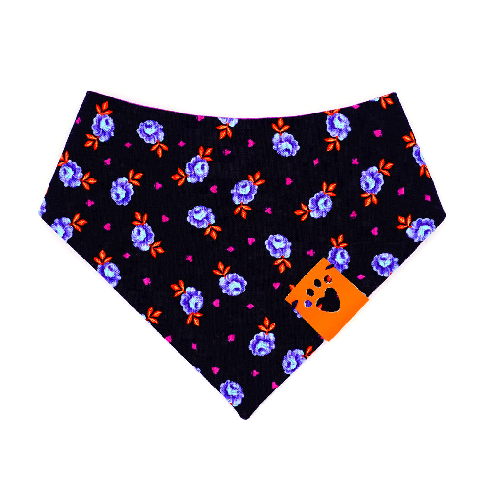 Reversible bandana for dogs. Snaps on back make it adjustable. One side is Navy blue background with purple and light blue rose buds, bright orange leaves and bright purple accent shapes and the other side has Bright purple background with bright orange dots. Orange tag with heart paw cut out on side.