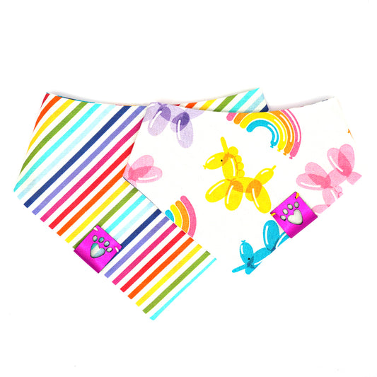 Reversible bandana for dogs. Snaps on back make it adjustable. One side is White background with rainbow stripes and the other side has a White background with rainbow-colored balloon animals and rainbows. Metallic Pink tag with heart paw cut out on side.