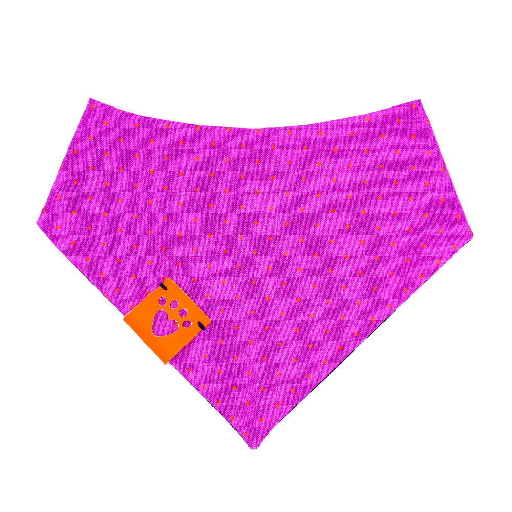 Reversible bandana for dogs. Snaps on back make it adjustable. One side is Navy blue background with purple and light blue rose buds, bright orange leaves and bright purple accent shapes and the other side has Bright purple background with bright orange dots. Orange tag with heart paw cut out on side.