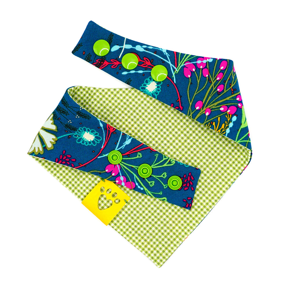 Reversible bandana for dogs. Snaps on back make it adjustable. One side is Dark green/teal background with magenta, dark purple, lime green, white, light blue, goldenrod, and orange flowers and the other side has a Bright lime green and white gingham pattern. Yellow tag with heart paw cut out on side.