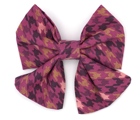 Handmade cotton bow tie with tails for dogs (or other pets). Elastic straps on back with snaps make it easy to add to collar, harness, or leash. Pink background with gold, maroon and light pink houndstooth pattern.