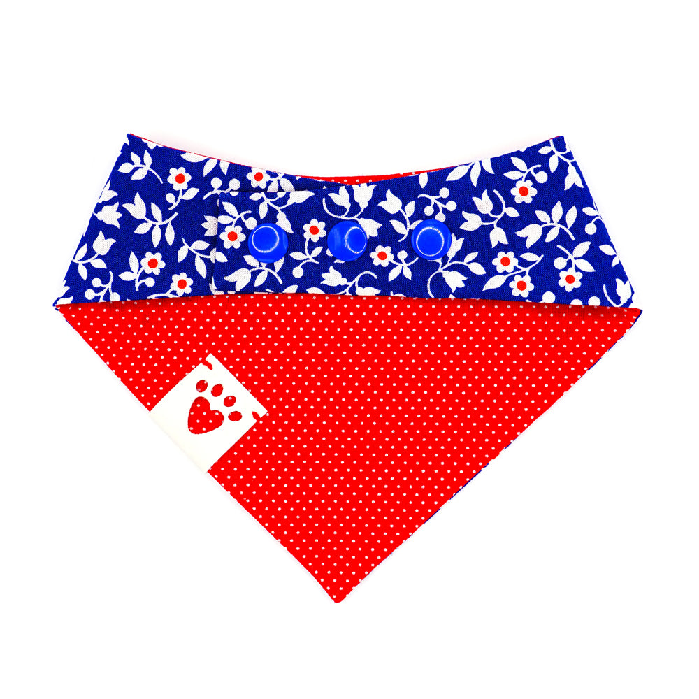 Reversible bandana for dogs. Snaps on back make it adjustable. One side is Medium blue background with red and white flowers and the other side has a Bright red background with white polka dots. White tag with heart paw cut out on side.