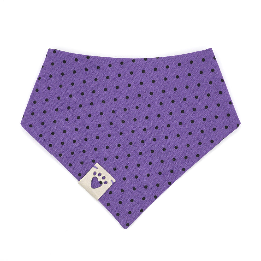 Reversible bandana for dogs. Snaps on back make it adjustable. One side is Black background with white flying ghosts and the other side has a Purple background with black polka dots. Light Grey tag with heart paw cut out on side.