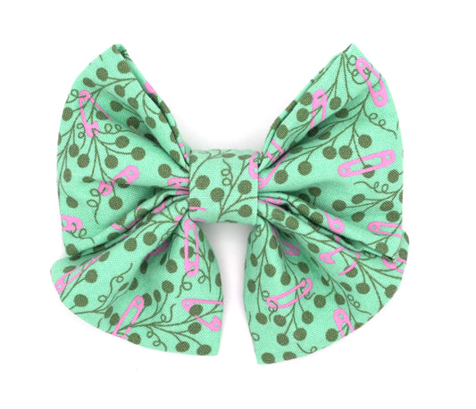Handmade cotton bow tie with tails for dogs (or other pets). Elastic straps on back with snaps make it easy to add to collar, harness, or leash. Teal green background with pink safety pins and dark green flowers.