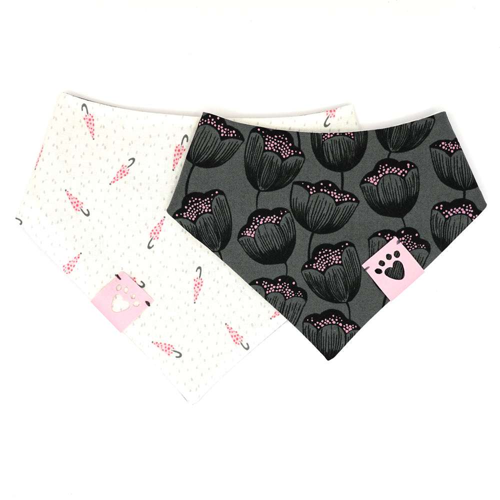 Reversible bandana for dogs. Snaps on back make it adjustable. One side is White background with pink polk-a-dot umbrellas and grey dots and the other side has a Charcoal grey background with black and pink flowers. Light pink tag with heart paw cut out on side.