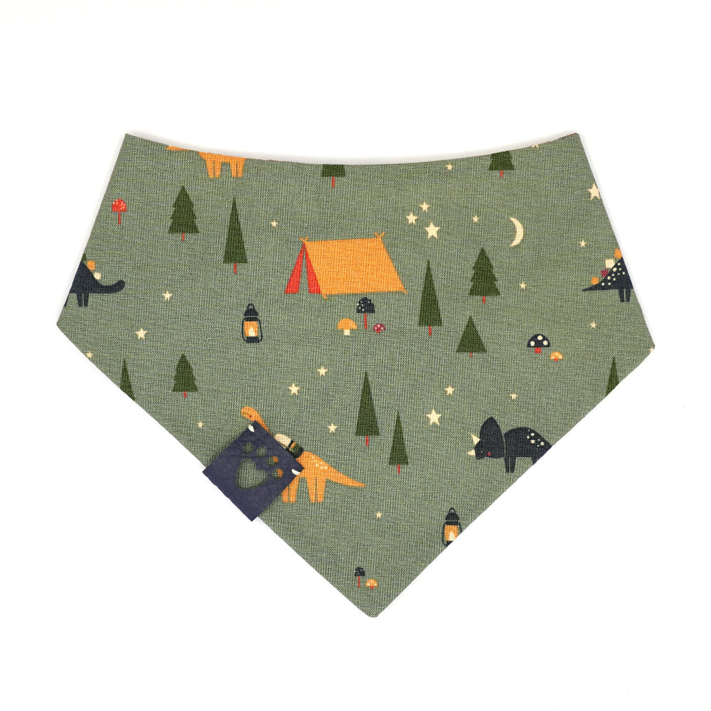 Reversible bandana for dogs. Snaps on back make it adjustable. One side is Army green background with tan, navy and orange dinos, tents, trees, lanterns and mushrooms and the other side has a Cream background with navy, forrest green, gold, red and brown plaid stripes. Navy tag with heart paw cut out on side.