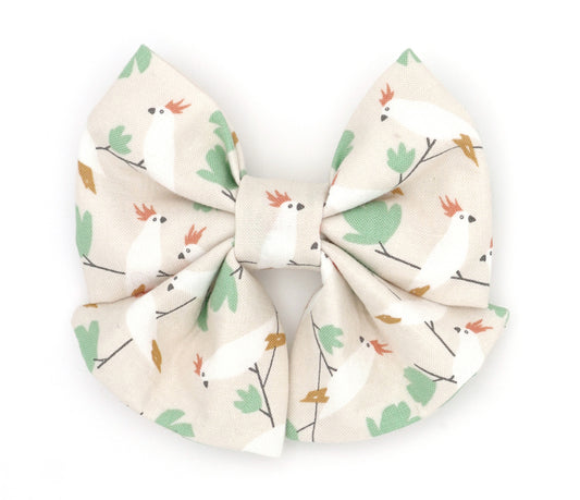 Handmade cotton bow tie with tails for dogs (or other pets). Elastic straps on back with snaps make it easy to add to collar, harness, or leash. Beige background with white, orange and green cockatiel birds