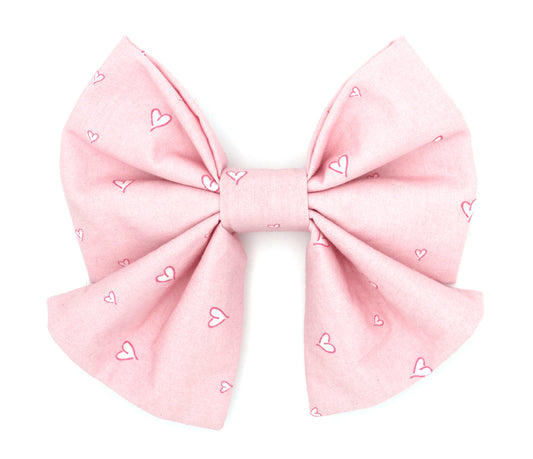 Handmade cotton bow tie with tails for dogs (or other pets). Elastic straps on back with snaps make it easy to add to collar, harness, or leash. Light pink background with hot pink and white hearts.