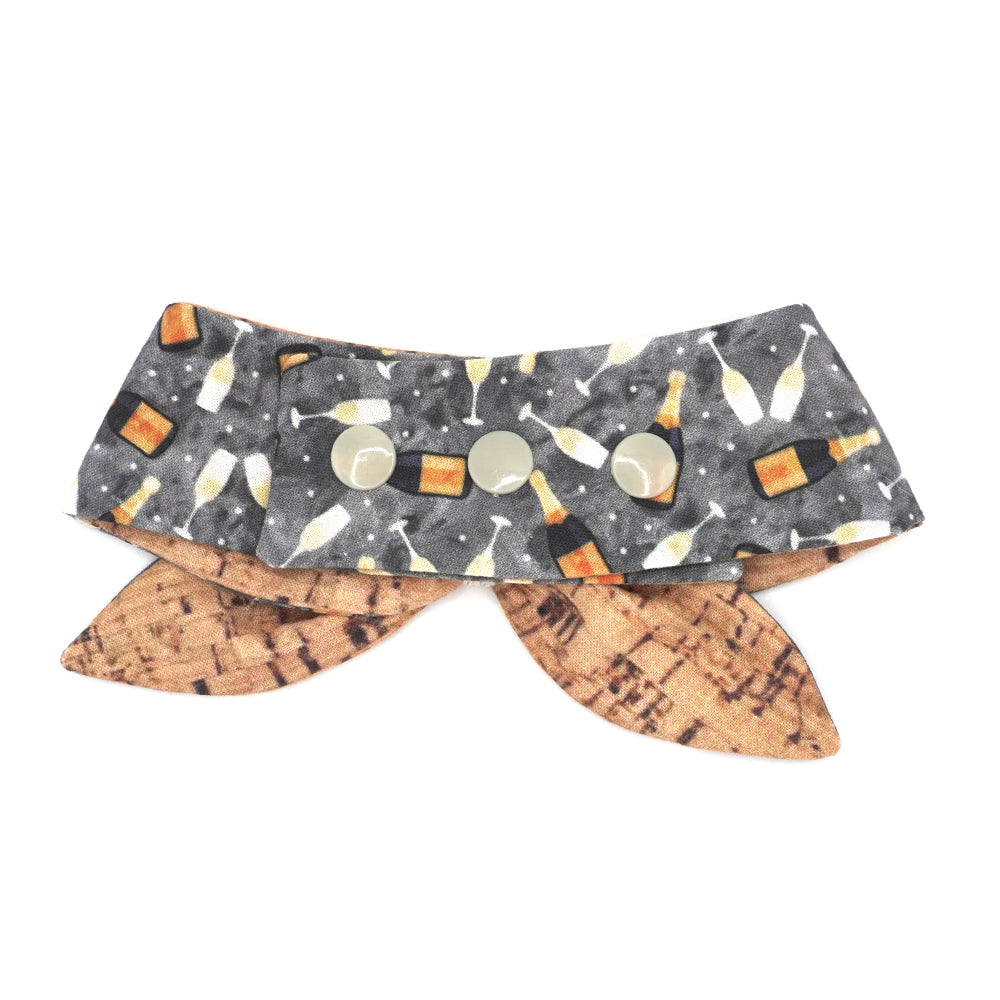Reversible neckerchief for dogs. Snaps on back make it adjustable. One side is Grey background with sparkling wine bottles and glasses and the other side has a Tan/brown cork pattern. Embroidery thread wrapped center in cream.