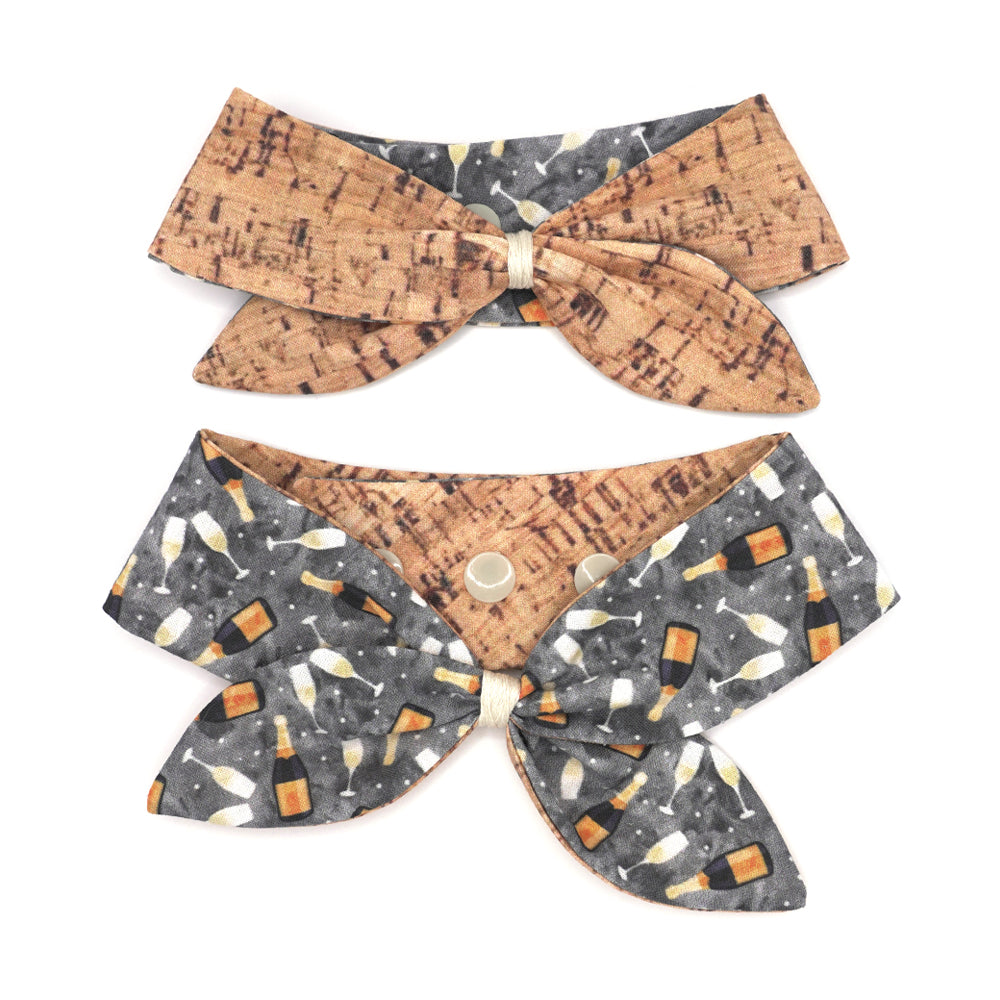 Reversible neckerchief for dogs. Snaps on back make it adjustable. One side is Grey background with sparkling wine bottles and glasses and the other side has a Tan/brown cork pattern. Embroidery thread wrapped center in cream.