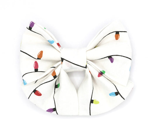 Handmade cotton bow tie with tails for dogs (or other pets). Elastic straps on back with snaps make it easy to add to collar, harness, or leash. White background with rainbow-colored lights on a black cord.