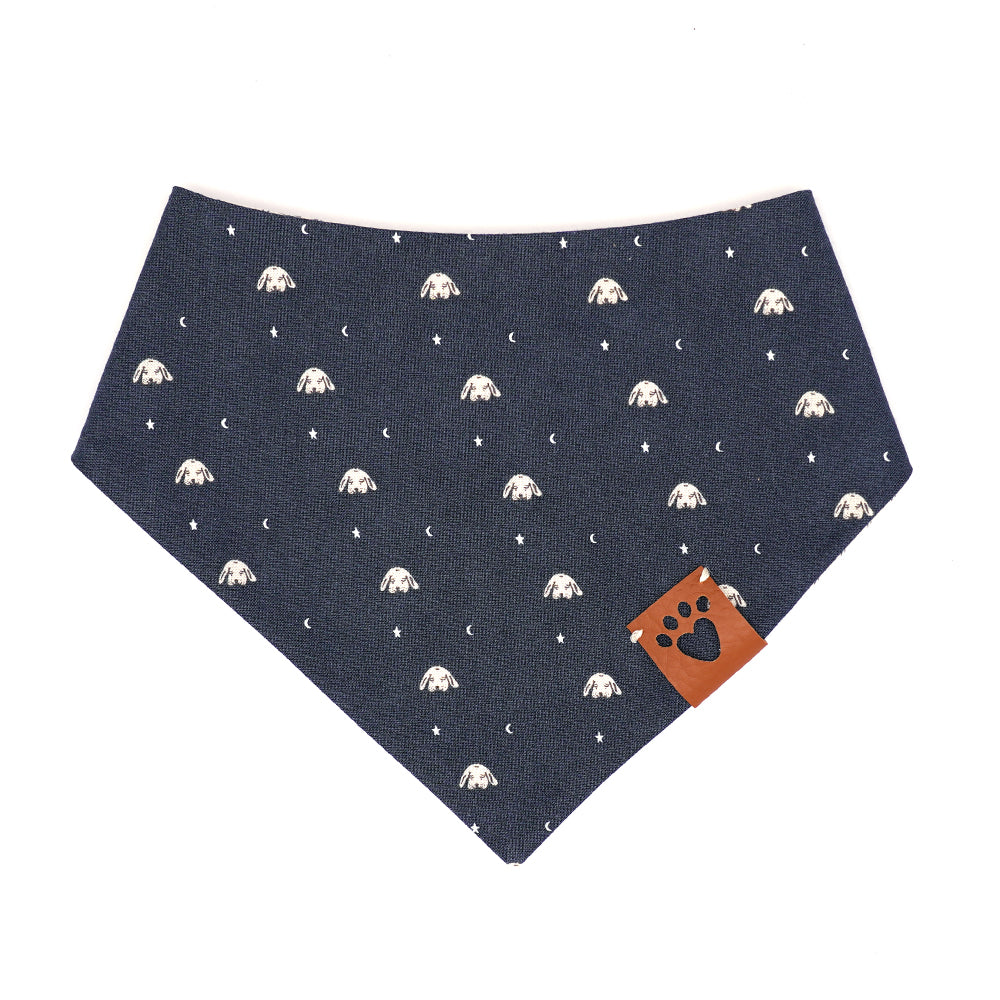 Reversible bandana for dogs. Snaps on back make it adjustable. One side is Navy blue background with tan illustrated dog heads, moons and stars and the other side has a Cream background with black illustrated bones (very pale blue inside bone). Tan tag with heart paw cut out on side.