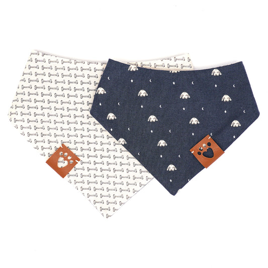 Reversible bandana for dogs. Snaps on back make it adjustable. One side is Navy blue background with tan illustrated dog heads, moons and stars and the other side has a Cream background with black illustrated bones (very pale blue inside bone). Tan tag with heart paw cut out on side.